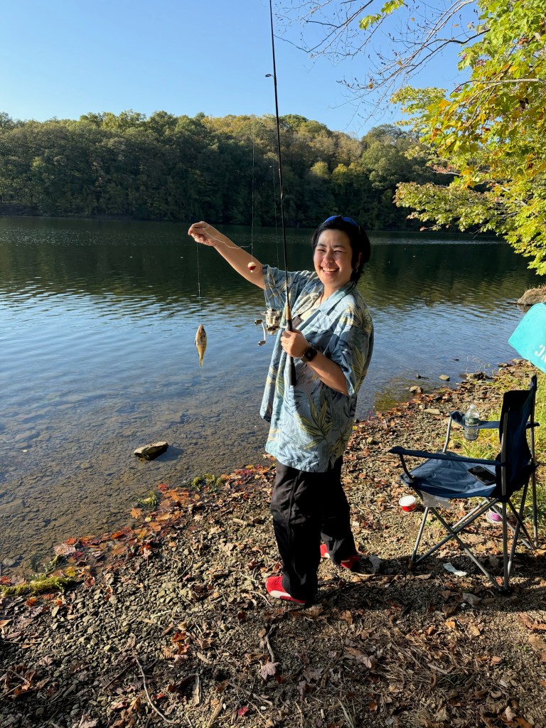 Person holding a fishing rod with a caught fish in a serene lakeside setting.
